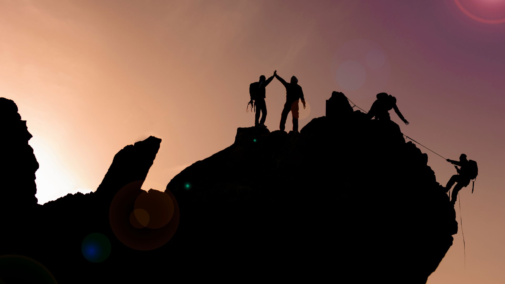 A figure silhouetted at the summit of a mountain at sunrise